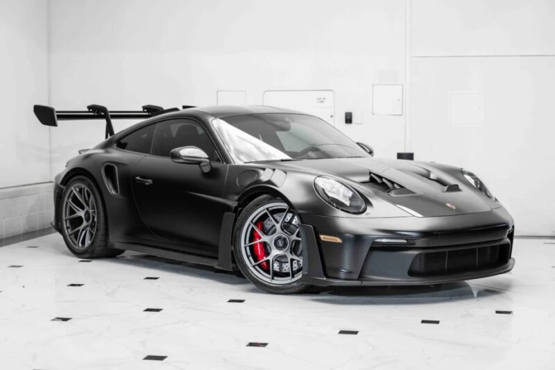 A sleek black 2023 Porsche 911 GT3 RS with a prominent rear spoiler, red brake calipers, and aerodynamic design rests on a white tiled floor.