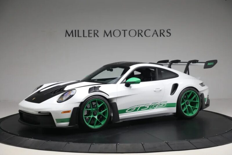 A sleek, white Porsche 911 GT3 RS with striking green accents and the iconic "GT3 RS" logo graces the showroom floor of Miller Motorcars. The 2023 Porsche model is a testament to style and performance, offering an irresistible opportunity for those looking to buy a Porsche.