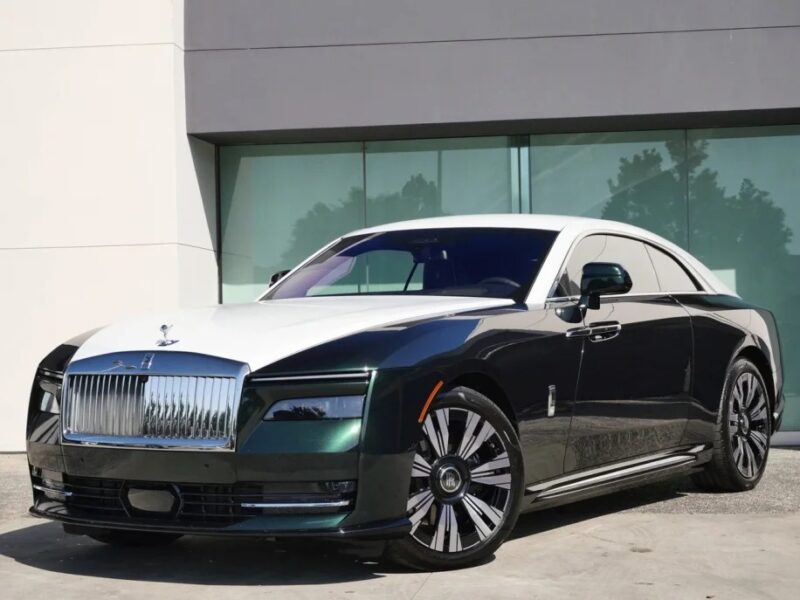 An ultra-luxe black and white Rolls-Royce Spectre is elegantly parked in front of a modern building with large windows, epitomizing the fusion of opulence and cutting-edge innovation.