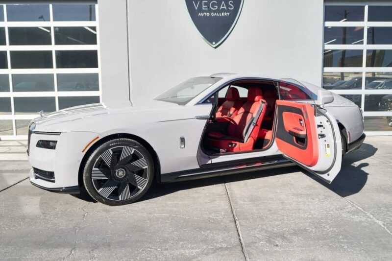 A Rolls-Royce with a red interior and open front door is parked in front of a building labeled "Vegas Auto Gallery," exuding ultra-luxe charm.