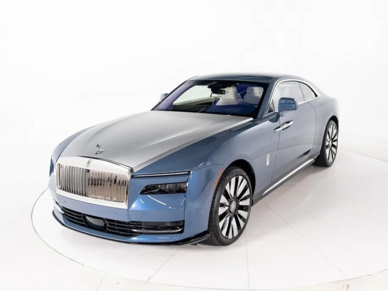 A blue and silver Rolls-Royce Spectre graces the scene, exuding Ultra-Luxe elegance against a pristine white background.