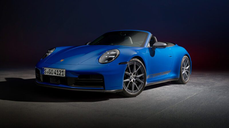 Blue sports car with convertible top, silver wheels, and prominent front headlights, parked on a dark surface.