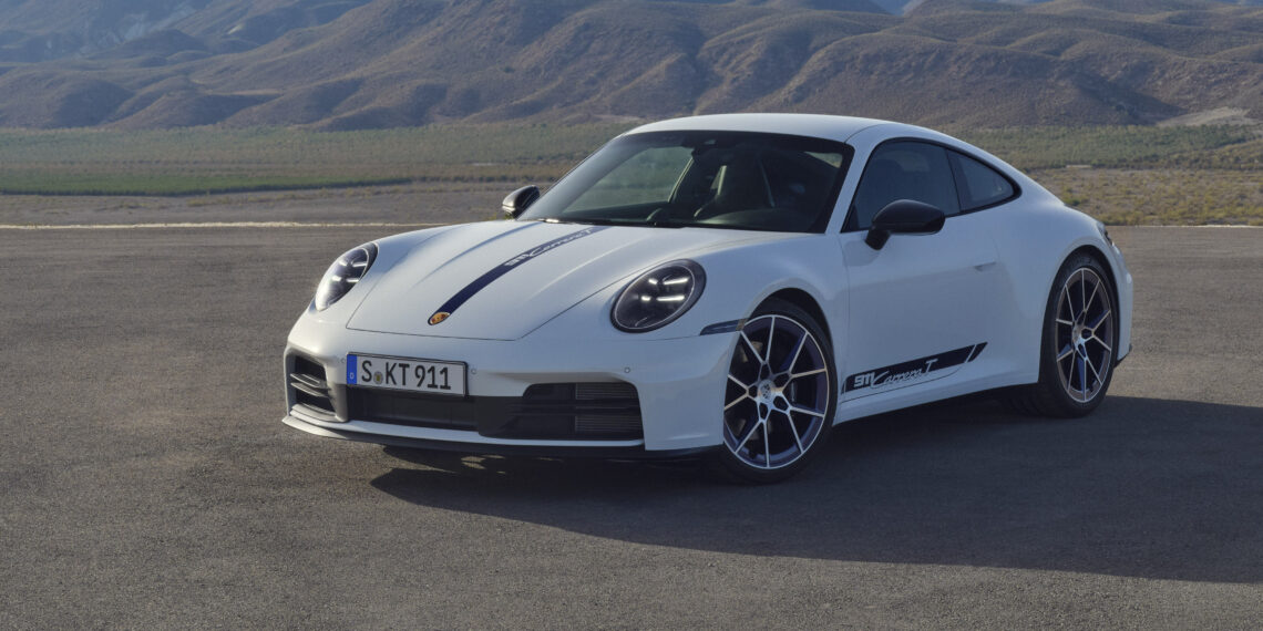 A white sports car is parked on a paved surface with mountainous terrain in the background.