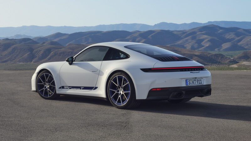 A white sports car is parked on an open road with mountains in the background.