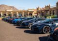 A lineup of hypercars including a stunning Bugatti is parked in front of the grand building, with majestic mountains serving as the perfect backdrop for this luxurious tour.