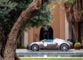 A luxury hypercar is parked beside a tree, near a shimmering pool, with a grand building and swaying palm trees providing a stunning backdrop reminiscent of Morocco's exotic allure.