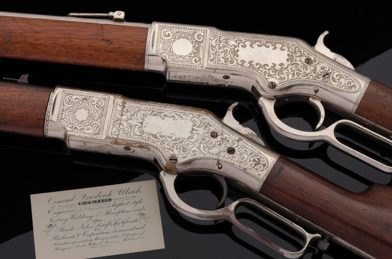 Two ornately engraved Colts lever-action rifles with silver detailing are displayed on a black surface, exuding an air of sophistication akin to a Concours d'Elegance, alongside a business card.