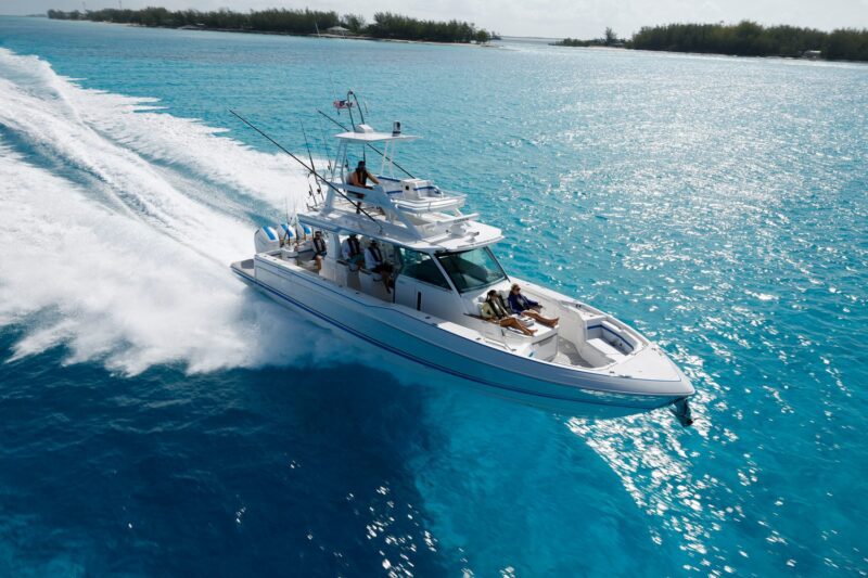 A luxury motorboat speeds across clear blue water, leaving a wake behind. The ocean and distant shoreline are visible under the sunny sky, evoking the thrill of the 2024 Fort Lauderdale International Boat Show.