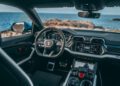 Interior view of the lavish Lamborghini Urus showcases a sleek steering wheel and cutting-edge digital dashboard, paired with an ocean view through the front windshield—an experience that epitomizes elegance and innovation.