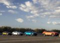 Four colorful cars, including a sleek Lamborghini Urus, parked in a row on a road under the cloudy Nardò sky.