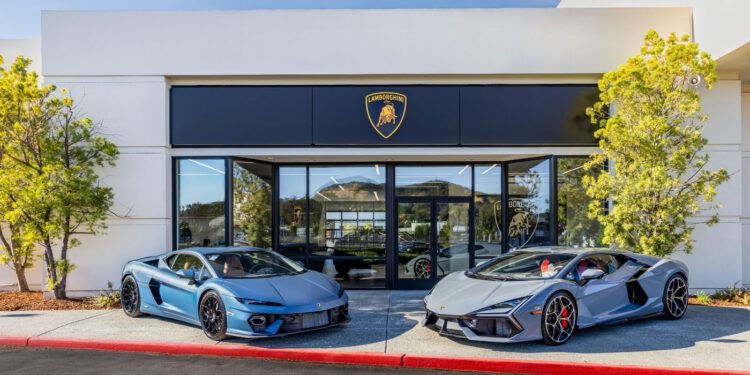 Two silver sports cars are parked in front of a building adorned with the Lamborghini logo. It's a clear sign of an exclusive VIP event at the San Francisco showroom.