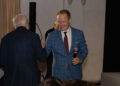 At the 2024 Autostyle Design Competition in Italy, a smiling man in a blue suit holds a microphone, shaking hands with another man wearing a dark jacket.