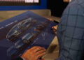 At the 2024 Autostyle Design Competition in Italy, a person signs a poster featuring sketches of a blue sports car, reminiscent of Lamborghini's iconic design elements.