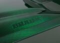 Close-up of a carbon fiber car body with a green tint, showcasing the word "BRABUS" embossed on the surface, enhances this Custom Mercedes-AMG G 63 with unmatched style and precision.