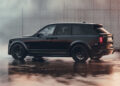 A black luxury BRABUS SUV with tinted windows is parked on a wet concrete surface next to a modern wall, exuding elegance and power.