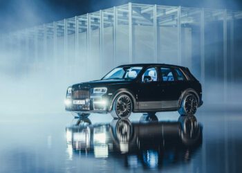 A black Rolls-Royce Cullinan is elegantly parked on a reflective surface in front of a modern architectural structure, enveloped by mist and dramatic lighting.