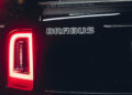 Close-up of a black car's rear with an illuminated red taillight, proudly displaying the "BRABUS" logo. This striking detail highlights the craftsmanship akin to a 700 Blue Sky design.