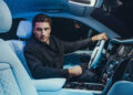 A man sits comfortably in the driver's seat of a Rolls-Royce Cullinan, enveloped by its illuminated starry ceiling and elegant interior lighting, epitomizing luxury.