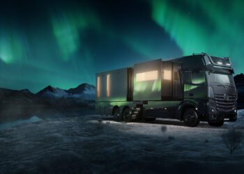 A BIG BOY 1200 truck with extended sections is parked in a snowy landscape under a vivid display of the Northern Lights.