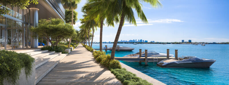 Waterfront view with a walkway lined by palm trees, steps leading to the path, and boats docked in a clear blue bay. The city skyline and Pagani Residences are visible in the distance under a bright blue sky, offering luxury services to those who appreciate elegance.