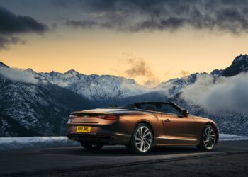 A brown Bentley Continental GT Speed is parked on a mountain road at sunset, overlooking snow-covered peaks and a cloudy sky, dreaming of the drive ahead powered by cutting-edge eFuels.