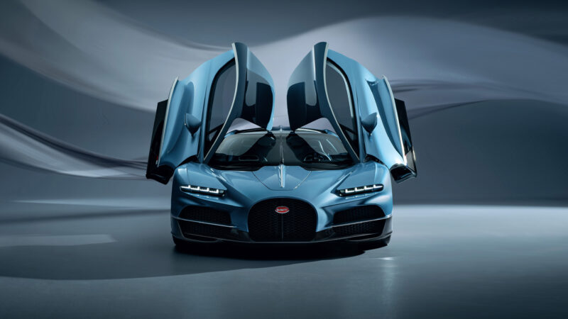 A sleek blue Bugatti sports car with vertically opening doors stands against a blurred background, showcasing its modern design and hinting at the next century of automotive innovation.