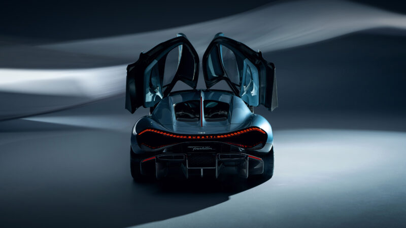 Sleek black Bugatti sports car with gull-wing doors open, viewed from behind against a dark, abstract background. Tail lights glow brilliantly, embodying the essence of the next century.