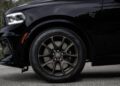 Close-up of a black Durango SRT's front wheel and fender, featuring a multi-spoke rim and high-performance tire with visible branding. The Brass Monkey accents add an extra touch of flair to this vehicle’s impressive design.