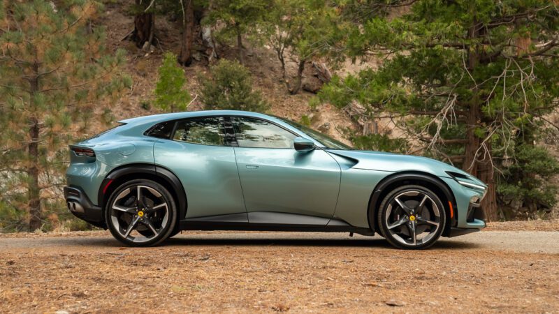 Sleek green sports car parked on a dirt road, surrounded by trees and rocky terrain.