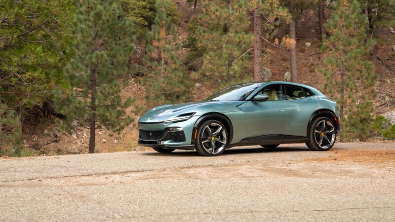 A sleek, blue luxury sports car parked on a road, surrounded by a forest with tall pine trees.