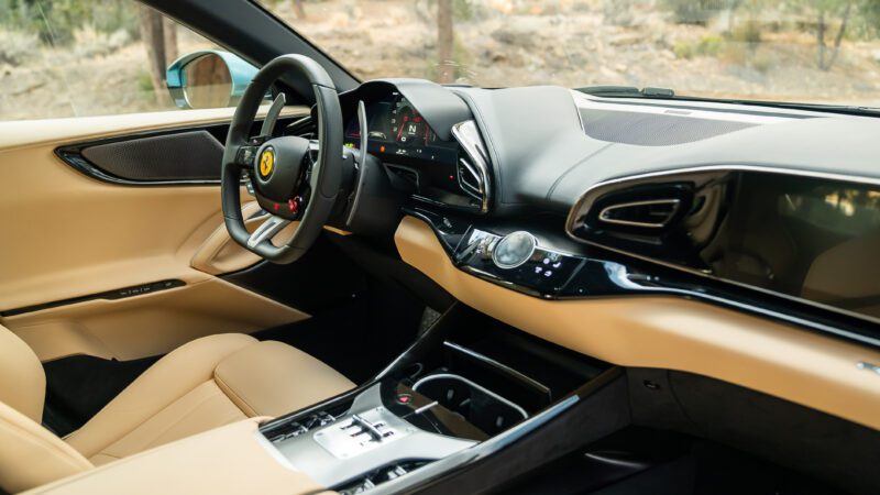 Interior of a luxury car showing a beige leather seat, modern dashboard, steering wheel with a logo, and digital displays.