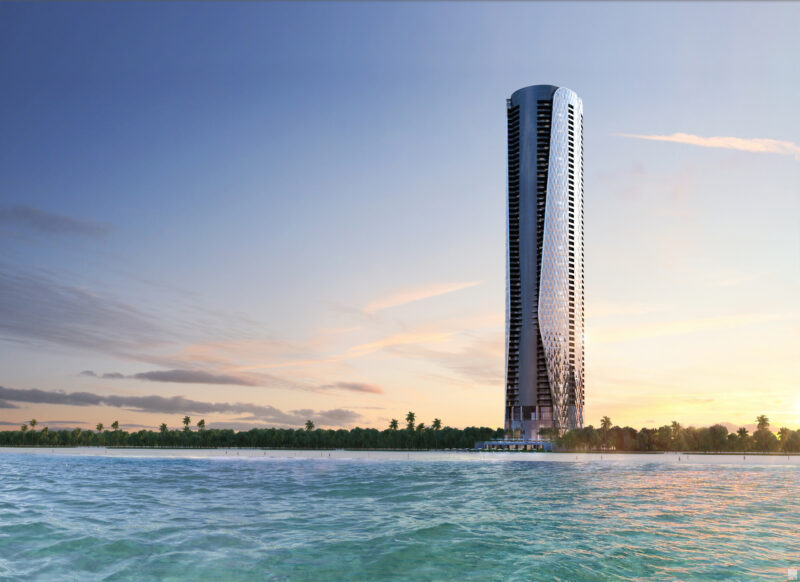 The towering, modern skyscraper of Bentley Residences stands majestically near a tranquil body of water, its sleek lines mirrored by the serene surface under a clear sky.