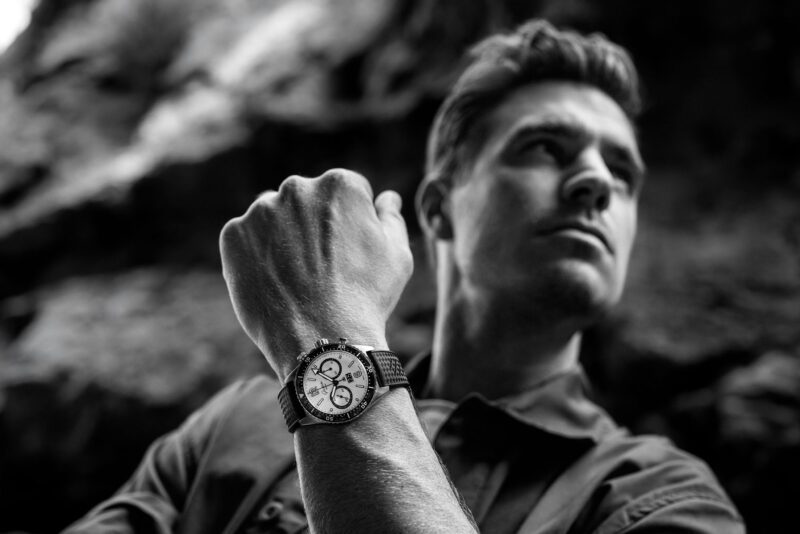 Black and white image of a man looking into the distance, with a close-up of his Glashütte Original wristwatch on his raised arm.