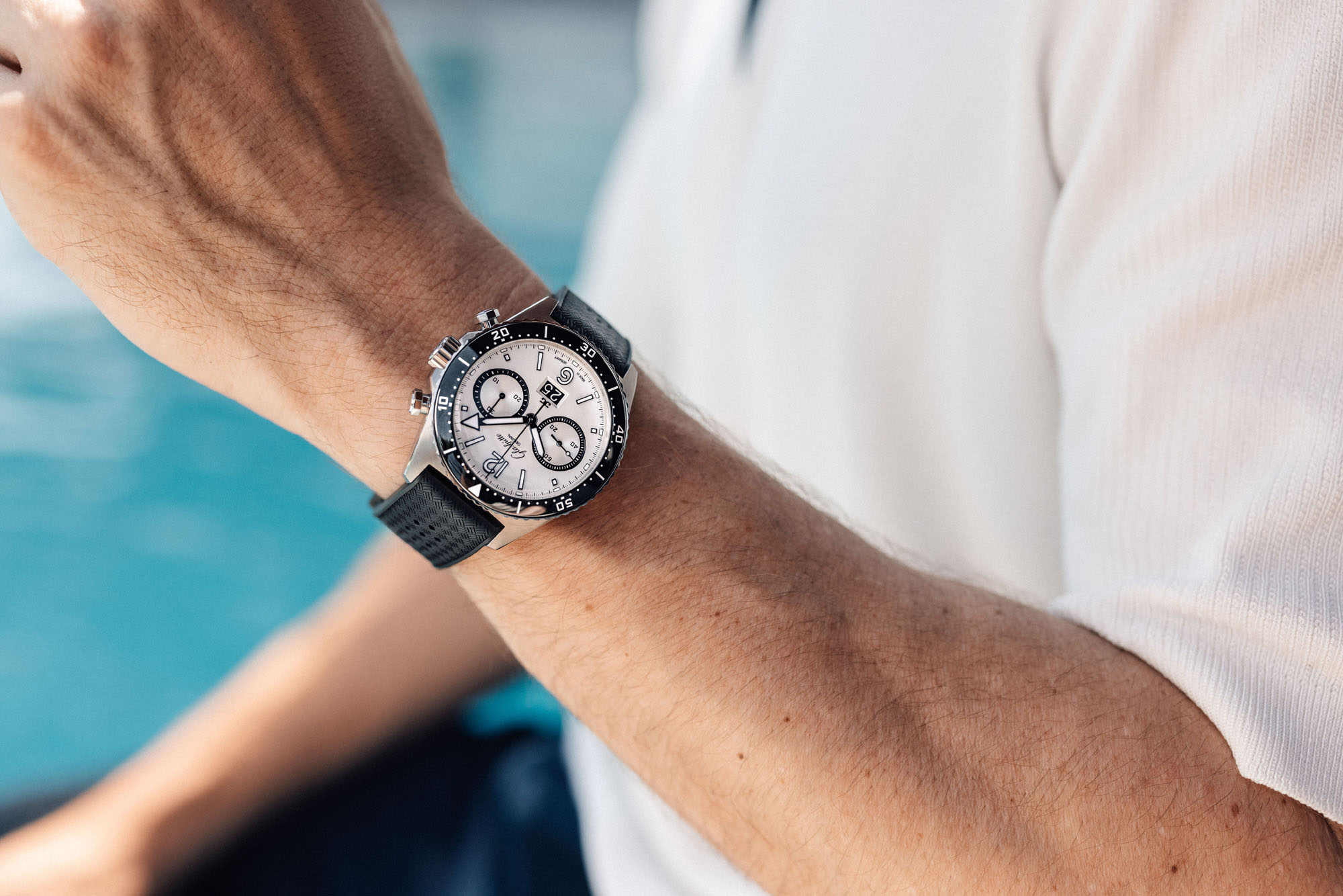 Close-up of a person wearing a SeaQ Chronograph, a luxury watch from Glashütte Original, featuring a silver face and black strap, near a pool.