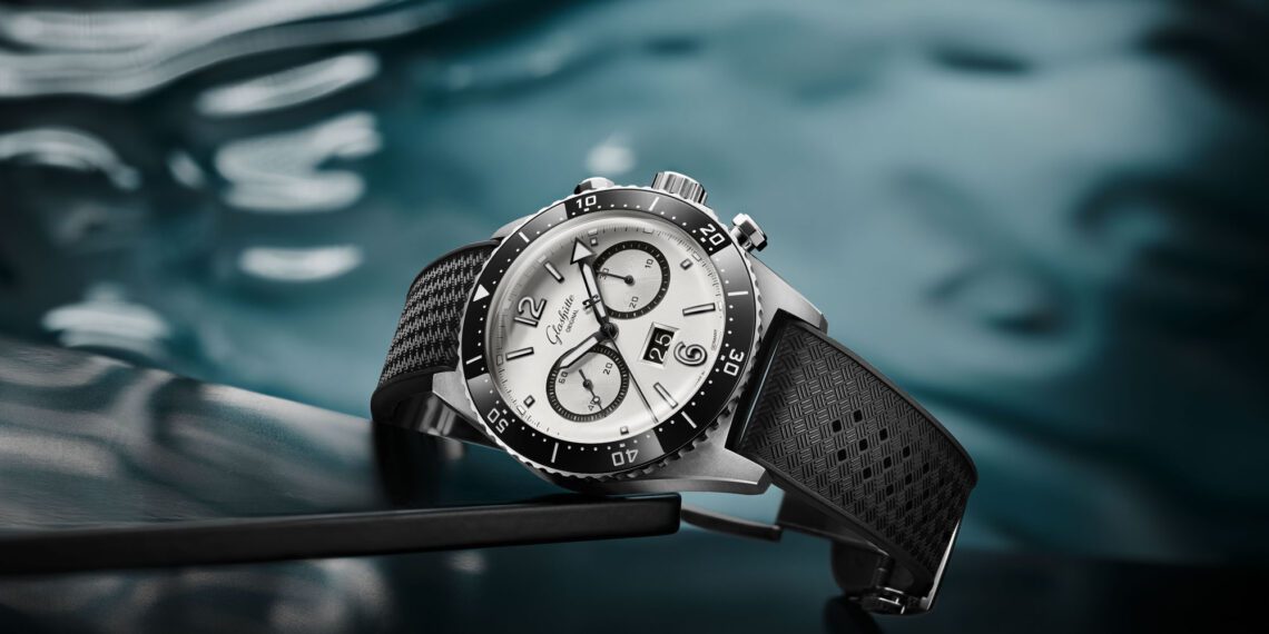 A new Chronograph wristwatch with a silver face and black strap rests elegantly on a reflective dark surface, complemented by its watery background.