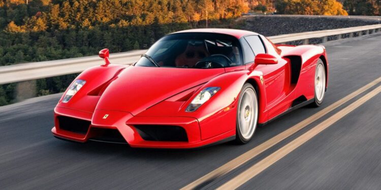 A sleek 2003 Ferrari in Rosso Corsa cruises down the road, with lush trees painting a vivid background.