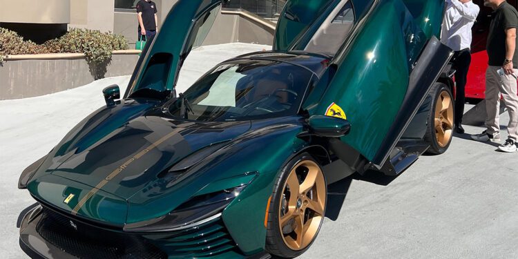 A dark green Daytona SP3 sports car with gold wheels and butterfly doors open, parked on a street with two people nearby, captivates the eye of a true Ferrari collector.