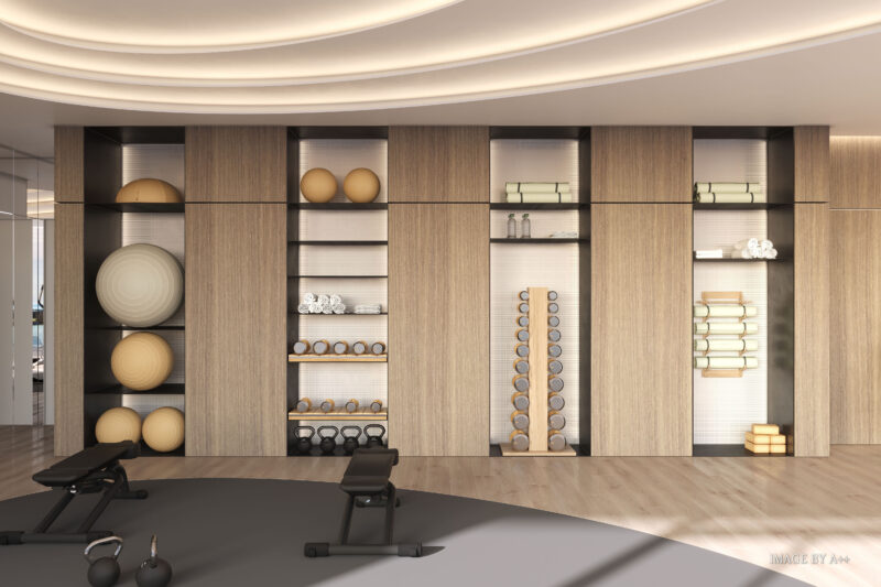 The modern gym interior at Pagani Residences features wooden shelves showcasing exercise balls, yoga mats, rolled towels, and various dumbbells. With two benches in the foreground, this space highlights the luxury services offered to residents without compromising on quality or style.