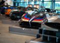 A lineup of luxury sports cars, including the stunning Pagani Zonda, is displayed indoors, each mounted on individual platforms.