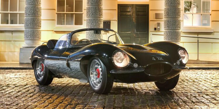A vintage 1957 Jaguar XKSS sports car is parked on a wet cobblestone street, with an elegant building in the background, its allure capturing the essence of classic luxury—an icon that once fetched $14 million at an RM Sotheby's Auction.