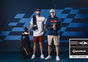 Two men in golf attire stand beside a golf bag adorned with the Pursuit Golf Collection. They wear TaylorMade branding and pose confidently in front of an Oracle Red Bull Racing backdrop, where a sign reads "Team Licensee.