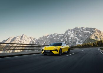 A yellow sports car zips along a mountain highway, with snow-capped peaks framed against a clear sky—a scene that feels as exhilarating as an auto draft on an open road.