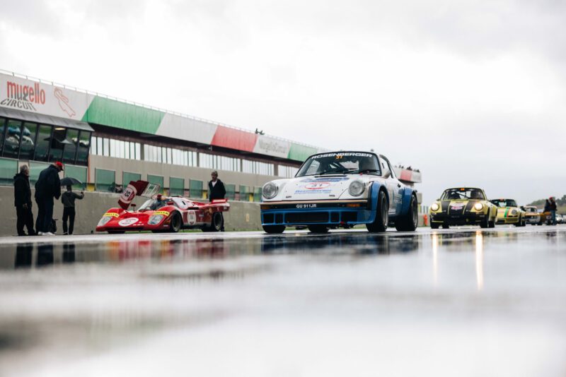 At the Modena Cento Ore's 2024 recap, vintage race cars lined up on a wet track at Mugello Circuit under overcast skies.