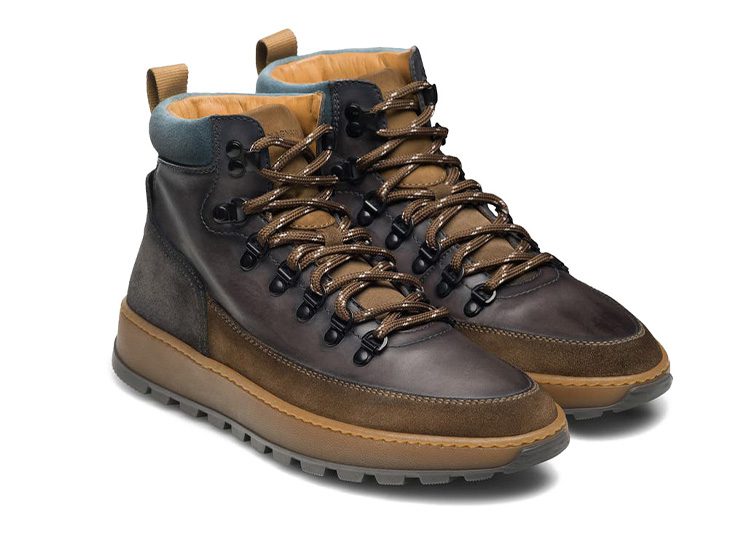 A pair of brown and olive high-top hiking boots with black eyelets and tan shoelaces on a gray rubber sole, perfect for the cooler months featured in the Fall Shopping Guide.