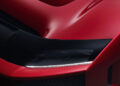 Close-up of a red hypercar's front end, highlighting the sleek black headlight and aerodynamic design reminiscent of a Ferrari.