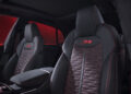 The interior of the Audi RS Q8 Performance showcases two black leather seats with red stitching and the "RS" logo. The textured center insert complements the dynamic look, set against a striking red background—a nod to its powerful combustion heritage.