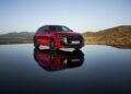 A red Audi RS Q8 Performance SUV sits on a reflective surface, framed by a stunning mountainous landscape in the background, perfectly embodying the powerful combustion that defines its Audi Sport model heritage.