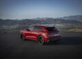 A striking red SUV, the Audi RS Q8, is parked on a scenic overlook with mountains in the background under a clear sky, showcasing its remarkable performance and power.