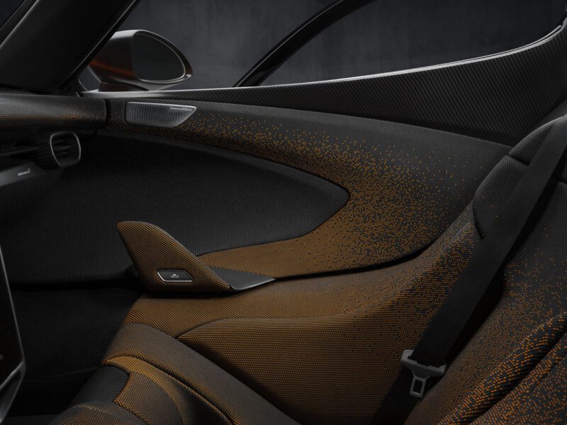 Close-up of the McLaren W1's interior showcasing sleek black and orange seats with a seatbelt, side panel, and window.