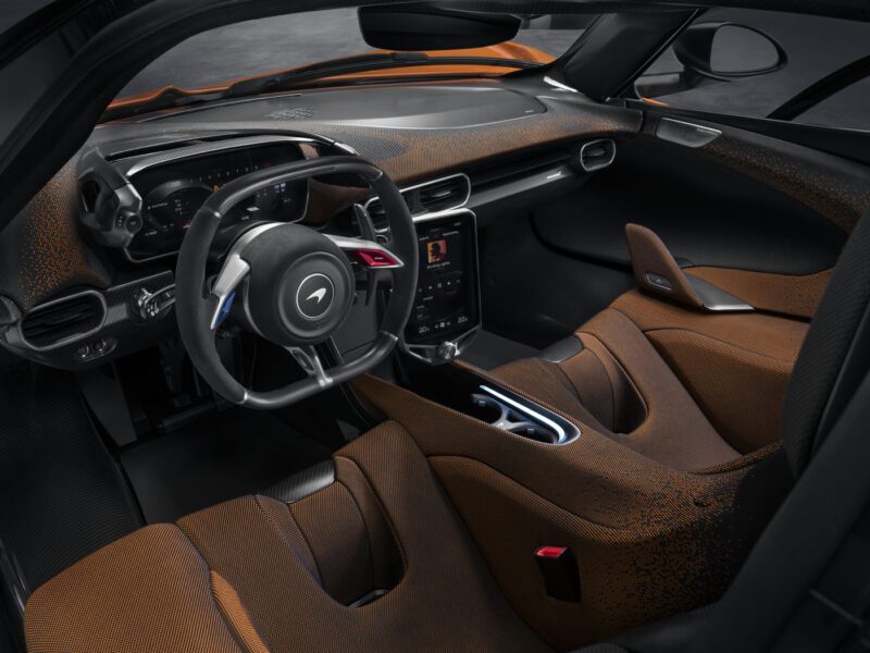 Interior view of a McLaren W1 luxury car featuring a sleek dashboard, digital display, and brown leather seats with a black steering wheel.